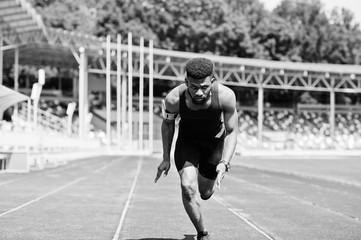 African american male athlete in sportswear racing alone down a running track at stadium.