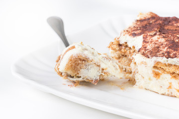 Slice of homemade tiramisu on a plate, on white background, side view. Main ingredients: ladyfingers, cream with mascarpone, cocoa powder, coffee, eggs