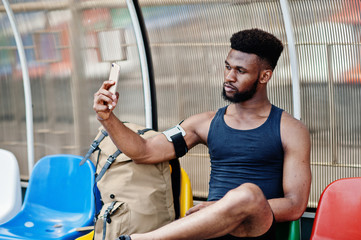 African american male athlete in sportswear with backpack sitting on chair at stadium and looking...
