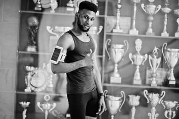 African american male athlete sexy sport man with running sports arm case for mobile phone, posed against many golden cups.