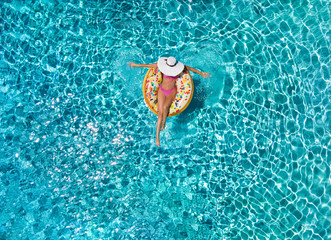 Entspannen im Urlaub: Frau mit Sonnenhut paddelt in einem schwimmenden Donut über blaues, klares Wasser