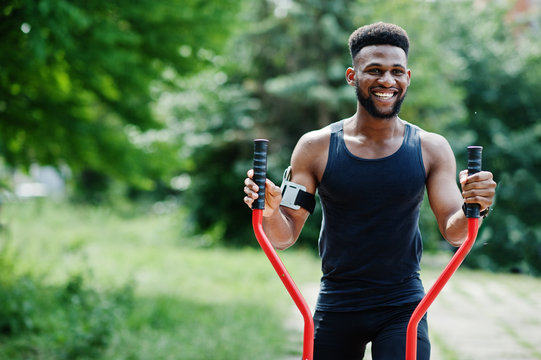 African american male athlete sport man with running sports arm case for mobile phone, doing exercises on the street workout simulators.