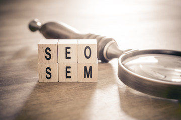 Old Magnifying Glass Lying Next to SEO And SEM Blocks In Monochrome Colors - Search Engine Optimization And Marketing Concept