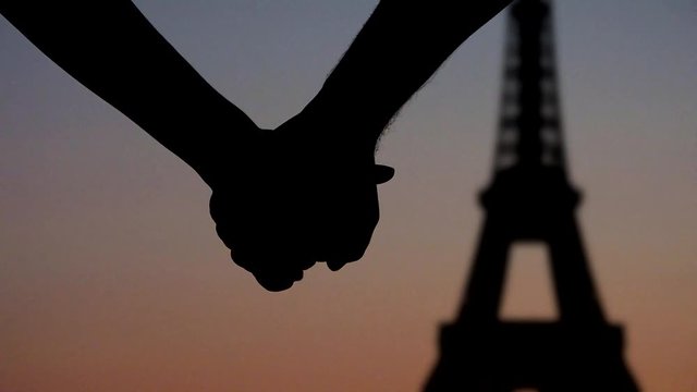 Young couple lovers joining hands in front of Eiffel tower Paris, silhouettes at sunset
