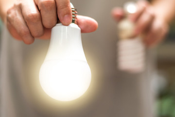 Power saving concept. Hands holding new Light Emitting Diode ( LED ) light bulb with light on and...
