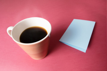 A cup of hot coffee and a postcar