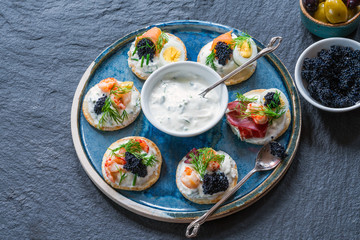 Selection of cocktail blinis with salmon, cured bresaola, crayfish, caviar, quail eggs and sour cream - gourmet party food - top view