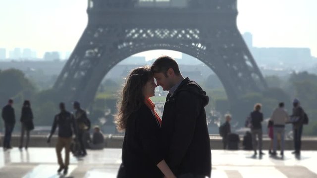 Lovers embrace in front of Eiffel tower, people passing