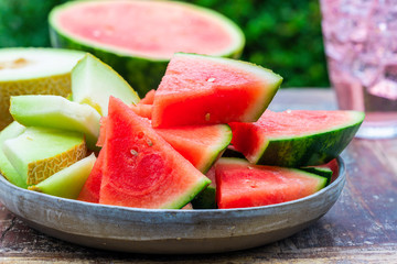 Slices of sweet, refreshing watermelon and honeydew melon on a garden table. Summer outdoor eating.