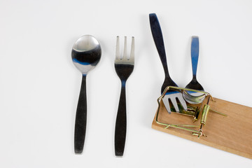 Cutlery and mousetrap on a white table. Fork and spoon caught in a trap.
