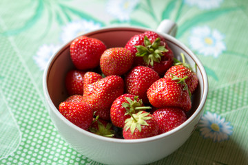 ripe strawberry berry with green leafs in a plate on a green background