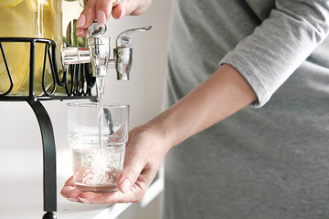 Female hands pour lemonade out of the tap of the dispenser.