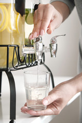 Female hands pour lemonade out of the tap of the dispenser.