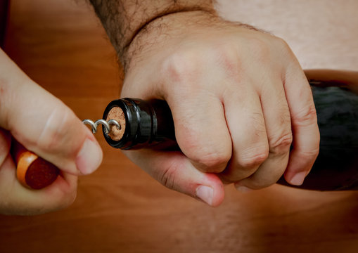 Close up. Men's hands pull the cork out of a bottle of wine with a corkscrew.