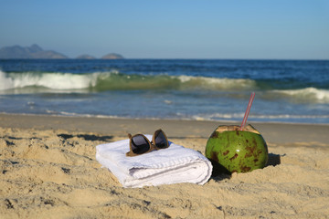 Sunglasses, towel and a fresh young coconut on the sandy beach with blurred Atlantic ocean in...