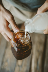 Man pouring milk in iced coffee