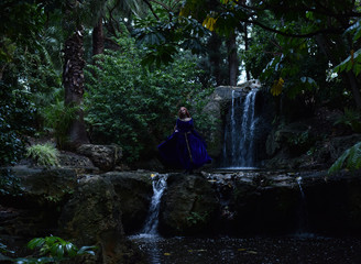 Fototapeta na wymiar full length portrait of girl wearing long blue medieval gown. wandering through a forest landscape.