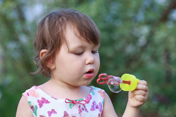 Cute little girl is blowing a soap bubbles.