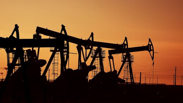 Many oil pumps at sunset under the red sky on industrial platform field with crude petroleum hydraulic extraction units