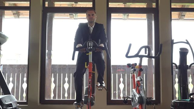 Man with suit training at static bicycle at gym, break at work