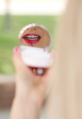 Fototapeta premium Young woman applying lipstick outdoors before an interview