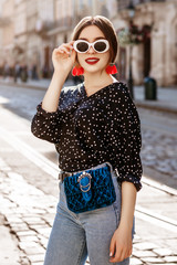 Outdoor portrait of young beautiful fashionable woman wearing stylish white oval sunglasses, red...