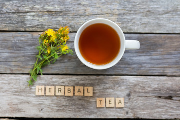 Cup of herbal tea and Hypericum - St Johns wort plant on wooden board table, top view.