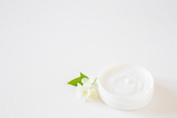 Opened jar of natural herbal cream for women on white table. Beautiful jasmine blossoms. Fresh flowers. Care about clean and soft face, hands, legs and body skin. Empty place for text or logo.