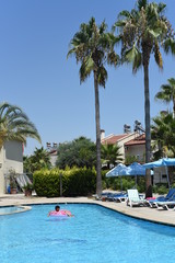 Happy cute little african-american boy lying on an inflatable donut circle  in the swimming pool in the hotel. Cool summer holidays for children and kids. Active games on the water.  Pink donat. 