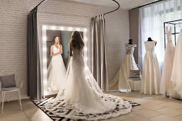 Gorgeous woman  in wedding salon is wearing a dress near loft mirror