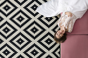 Gorgeous woman lays on the pink sofa in fashion wedding dress top view. Monochromic Scandinavian ornamet on background