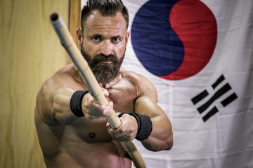 Hombre fuerte con grandes músculos entrenando artes marciales con arma han bo. Defensa personal...