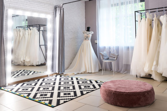  Collection of wedding dresses in the shop. Wedding salon interior. Large mirror