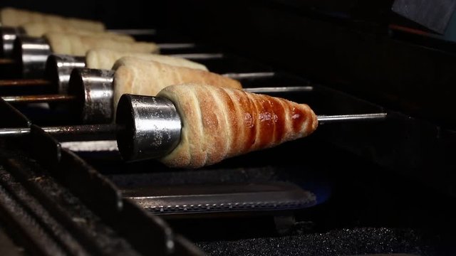 Close up sweet Trdelnik baking on grill and rolling, this spit cake is popular in Europe, Austria, Hungary, Slovakia and Czech, especially in Prague