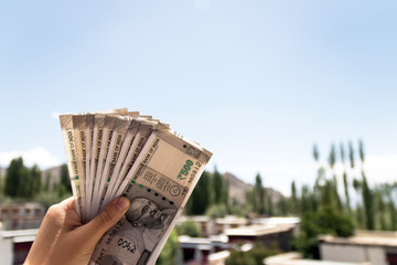 Hands holding new series Indian five hundred rupee notes with building of north India in background. Ready to travel and spend money for new experiences of life.