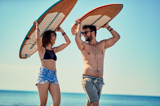 Surfers at the beach- Young couple of surfers walking on the beach and having fun in summer Vacation. Extreme Sport.
