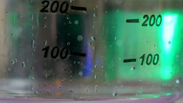 Transparent liquid drips into the measuring vessel with green back light close-up