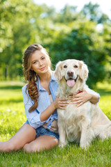 Young woman sitting on the grass with golden retriever dog in the summer park
