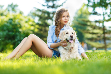 Young woman sitting on the grass with golden retriever dog in the summer park