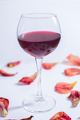 Red wine on a white background with rose petals