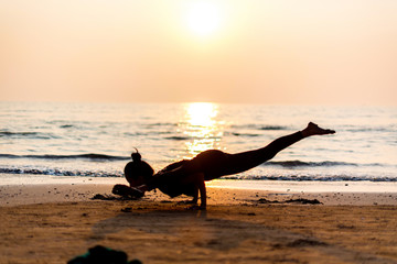 Young healthy woman practicing yoga on the beach at sunset