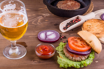 Fototapeta na wymiar Half empty glass of beer with delicious homemade hamburger