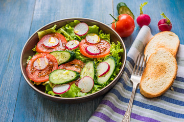 Healthy vegetarian salad with fresh tomatoes, cucumbers, onions, lettuce and radishes with olive oil on a rustic wooden background - top view