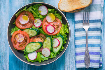 Healthy vegetarian salad with fresh tomatoes, cucumbers, onions, lettuce and radishes with olive oil on a rustic wooden background - top view