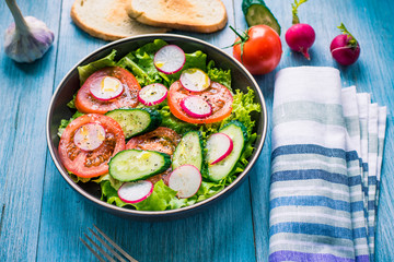 Healthy vegetarian salad with fresh tomatoes, cucumbers, onions, lettuce and radishes with olive oil on a rustic wooden background - top view