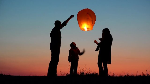 Parents, child and baby silhouette rising lightning sky lantern, conceptual release hope, free dreams of happy family