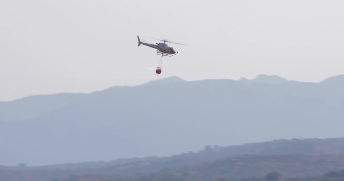 Elicottero antincendio con bambi bucket in volo per spegnere gli incendi nella foresta.