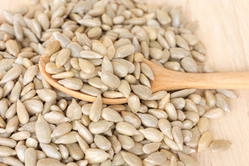 Sunflower seeds in wooden spoon on wooden board; nutrient background.