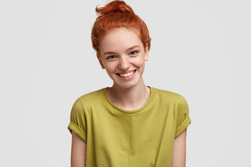 Positive ginger femae with freckled skin, broad smile, dressed in casual green t shirt, isolated over white background, expresses happiness as has date with boyfriend. Red haired teenager has weekend