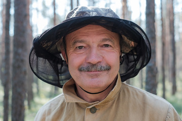 Portrait of a senior man in special hat against mosquito standing in forest.